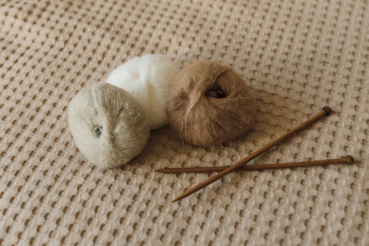 Fine woollen yarn balls and wooden knitting needles on a knitted surface