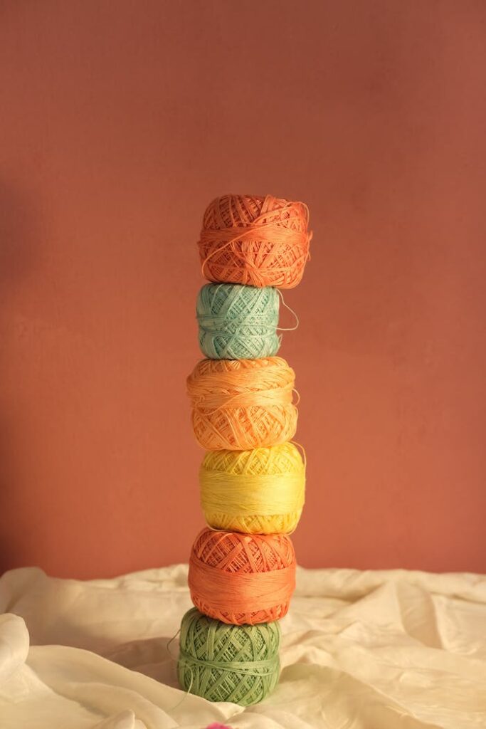 A vertical stack of colorful yarn balls on a red background with soft lighting.