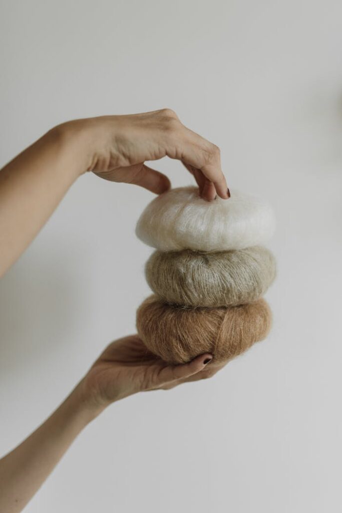 A close-up of hands gently holding three soft yarn rolls indoors.