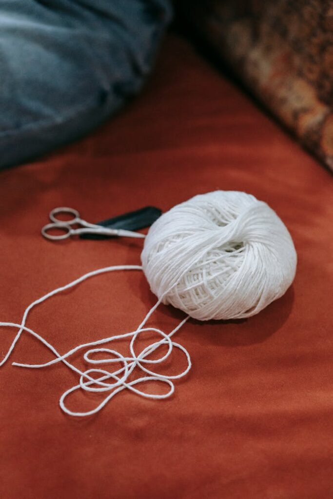 Close-up of a white yarn ball with scissors on a red textile surface, perfect for crafting themes.